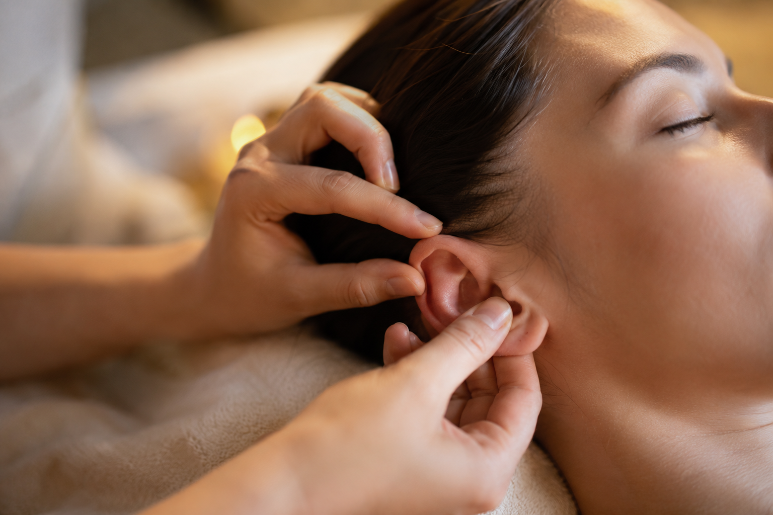 Gros plan sur un massage doux du pavillon de l'oreille en réflexologie auriculaire, ambiance sereine de bien-être
